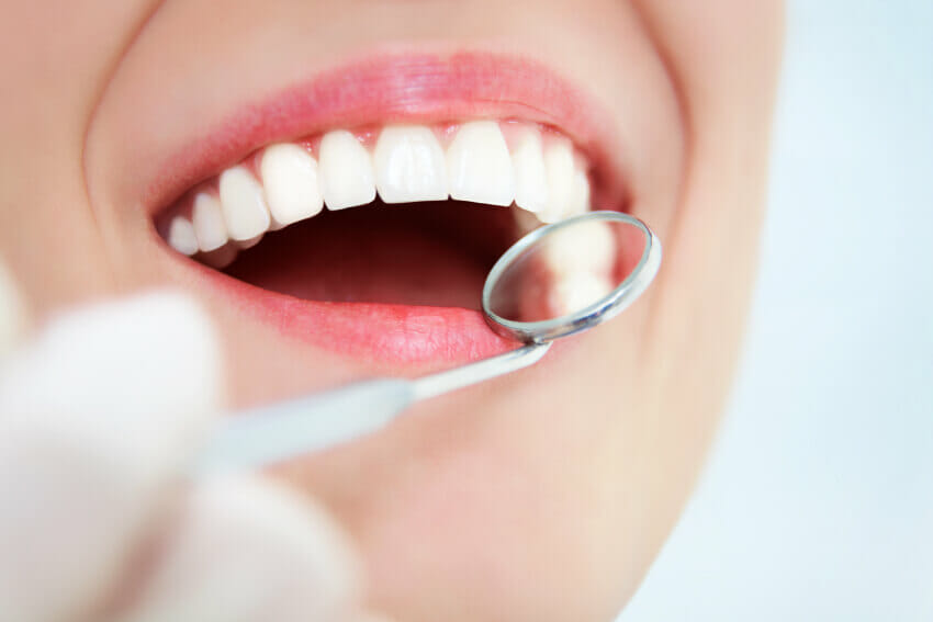 Dentist looking at woman's mouth with a hand mirror tool