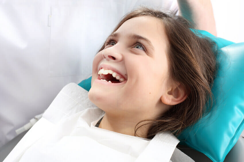 Young girl sitting in dental chair smiling awaiting her new sealants